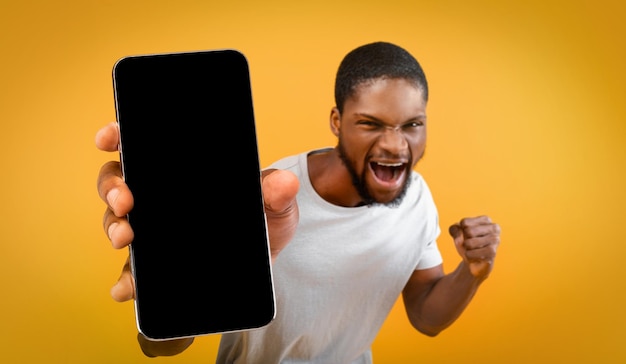 Hombre afroamericano emocional que muestra maqueta de teléfono inteligente