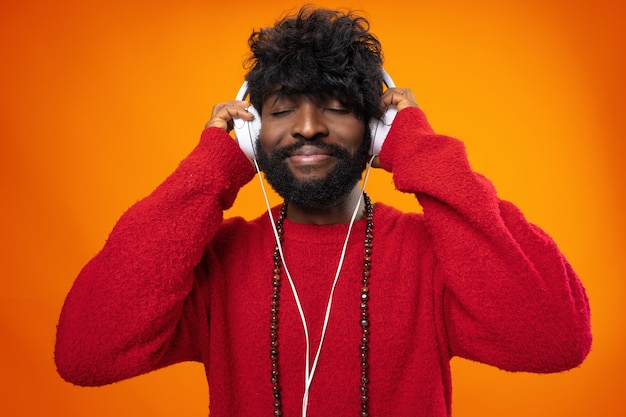 Hombre afroamericano escuchando música con alegría sobre fondo naranja