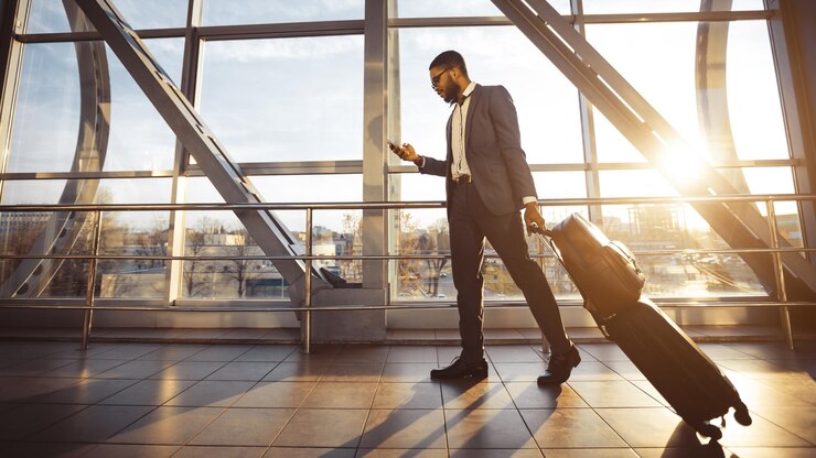 Foto un hombre afroamericano está usando su teléfono en una terminal del aeropuerto de pie con su equipaje el