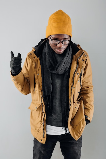 Hombre afroamericano con estilo joven con sombrero amarillo y chaqueta posando sobre fondo gris