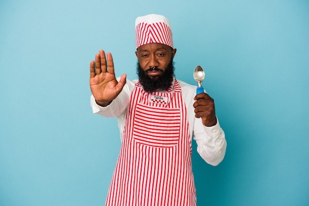 Hombre afroamericano fabricante de helados sosteniendo una bola de helado aislada sobre fondo azul de pie con la mano extendida mostrando la señal de stop, impidiéndote.