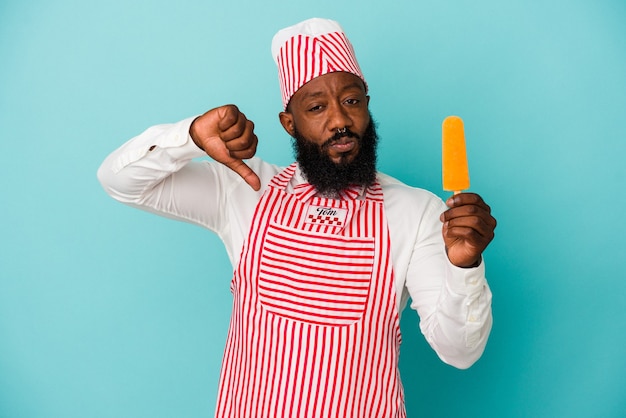 Hombre afroamericano fabricante de helados sosteniendo un helado aislado en la pared azul que muestra un gesto de aversión, pulgares hacia abajo. Concepto de desacuerdo.