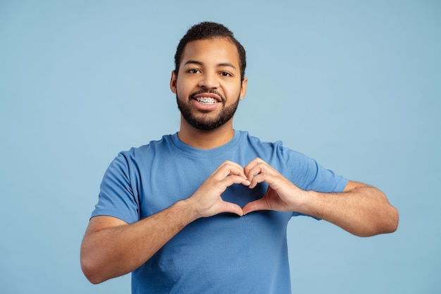 Hombre afroamericano feliz con aparatos ortopédicos que muestran la forma de un corazón para los suscriptores