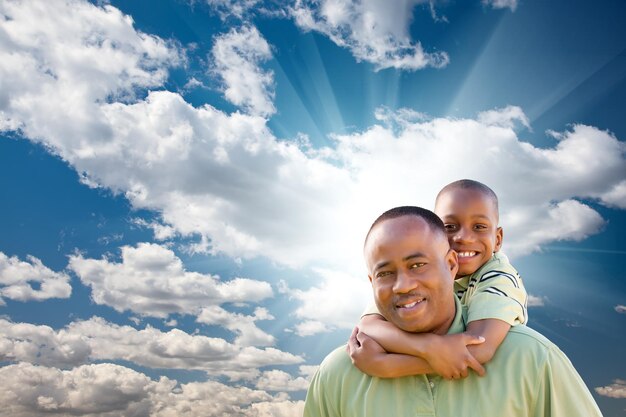 Hombre afroamericano feliz con un hijo sobre las nubes y el cielo