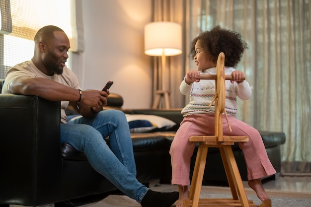 Hombre afroamericano feliz jugando con su hija en la sala de estar en casa