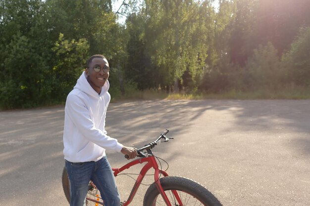 Un hombre afroamericano feliz y sonriente con una bicicleta en un parque público Deportes y recreación