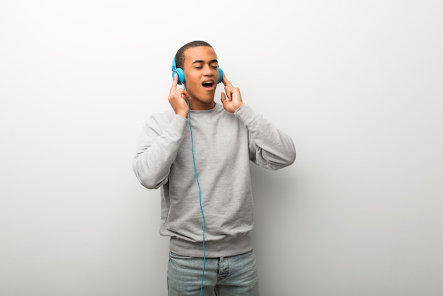 Hombre afroamericano en el fondo de la pared blanca escuchando música con auriculares