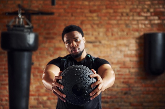 Hombre afroamericano fuerte con ropa deportiva en el gimnasio y sosteniendo la pelota en las manos