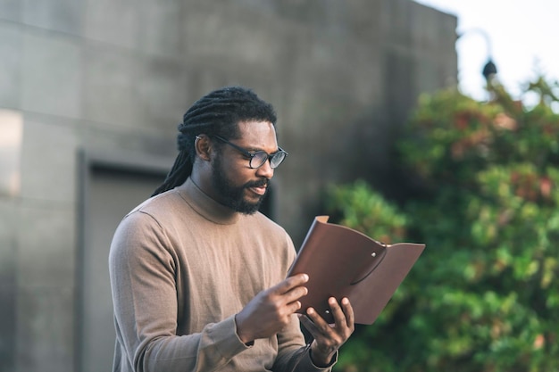 Hombre afroamericano con gafas leyendo en un parque