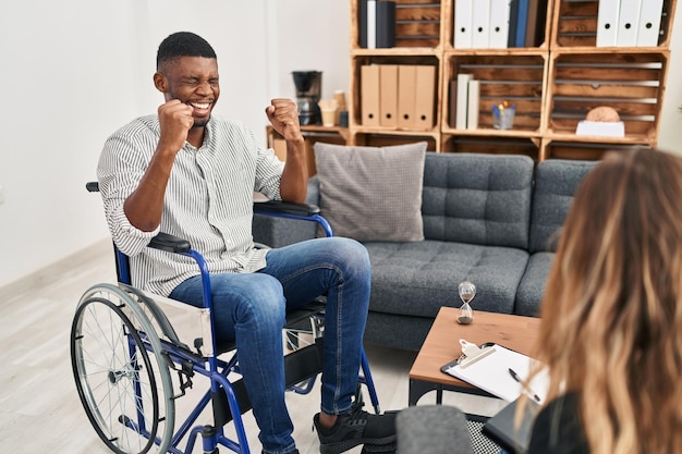 Hombre afroamericano haciendo terapia sentado en silla de ruedas emocionado por el éxito con los brazos levantados y los ojos cerrados celebrando la victoria sonriendo. concepto de ganador.