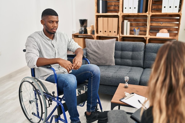 Hombre afroamericano haciendo terapia sentado en silla de ruedas relajado con expresión seria en la cara. mirada simple y natural a la cámara.