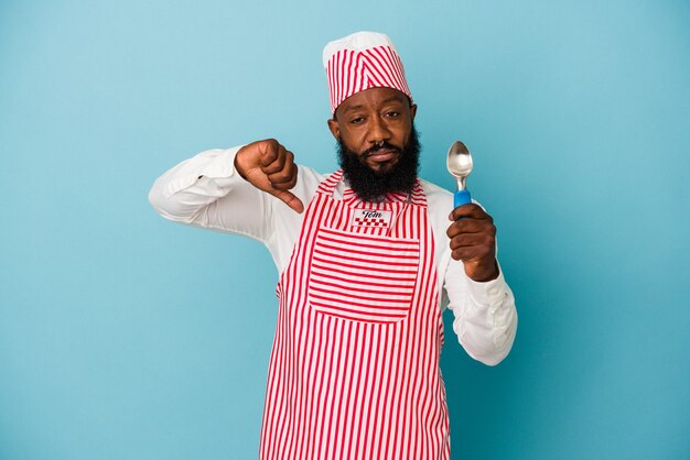 Hombre afroamericano helado sosteniendo una bola de helado aislada sobre fondo azul mostrando un gesto de aversión, pulgares hacia abajo. Concepto de desacuerdo.