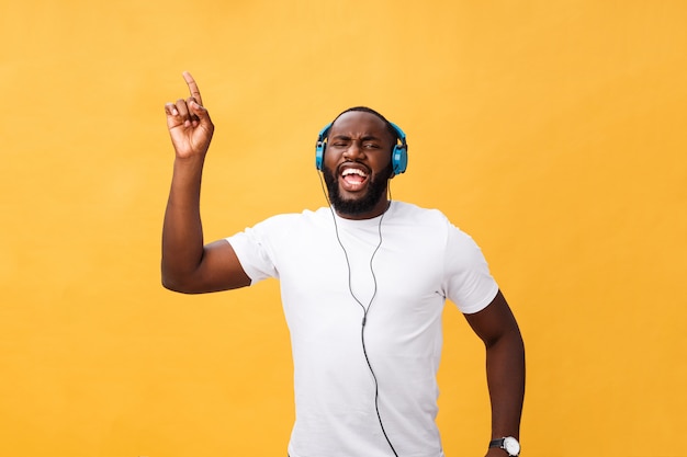 Hombre afroamericano joven con auriculares y disfrutar de la música bailando sobre fondo de oro amarillo