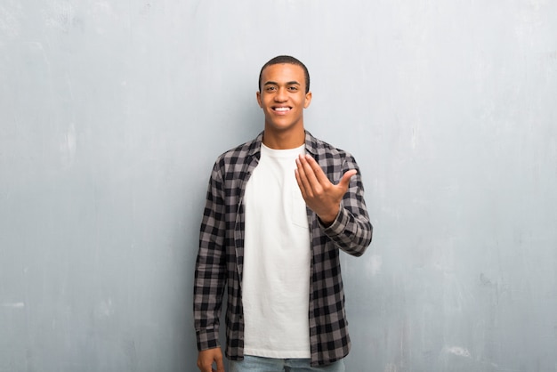 Hombre afroamericano joven con la camisa a cuadros que invita para venir con la mano.