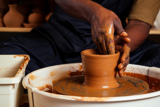 Hombre afroamericano joven y confiado en un delantal negro esculpe a un alfarero de un taller de alfarería de arcilla. olla de barro en la mano del artista latino