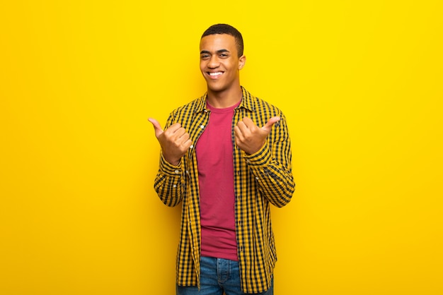 El hombre afroamericano joven en el fondo amarillo que da un pulgares arriba gesto con ambas manos y la sonrisa