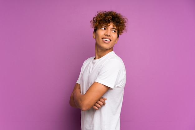 Hombre afroamericano joven sobre la pared púrpura aislada con los brazos cruzados y feliz