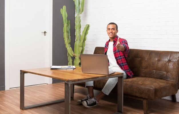 Hombre afroamericano con laptop en la sala de estar dándose la mano para cerrar un buen negocio