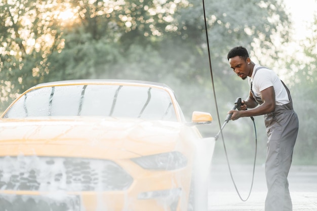 Hombre afroamericano lavando su auto bajo un chorro de agua a alta presión al aire libre