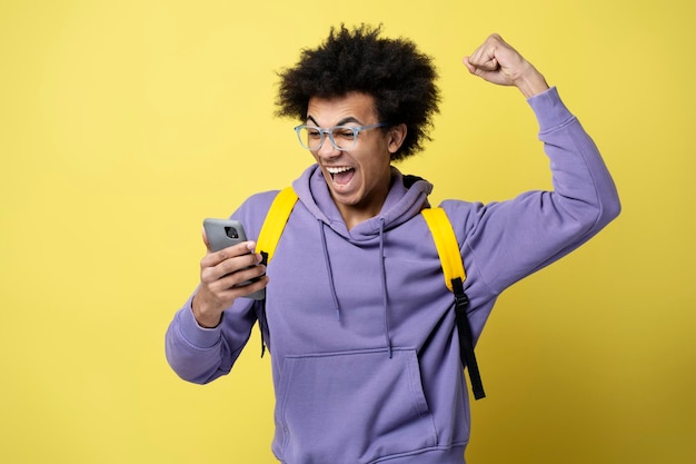 Hombre afroamericano lleno de alegría usando un teléfono inteligente jugando al éxito de la celebración del juego móvil