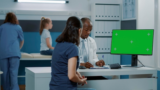 Hombre afroamericano y madre mirando la pantalla verde en el monitor del gabinete médico. especialista y mujer que usa computadora con plantilla de clave de croma, fondo de maqueta aislado y espacio de copia.