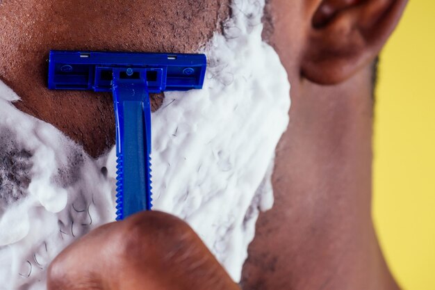 Hombre afroamericano con maquinilla de afeitar y espuma de afeitar en la cara