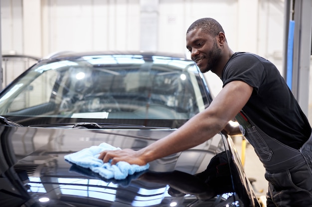 Hombre afroamericano mecánico de automóviles limpia la superficie perfecta de la máquina después de pulir