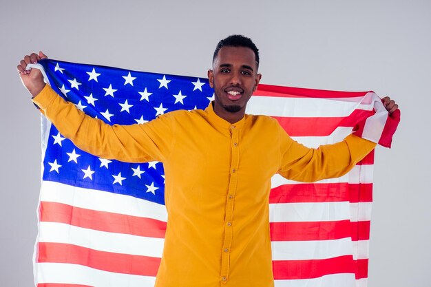 Hombre afroamericano mirando a la cámara y sosteniendo orgullosamente la bandera estadounidense en el estudio