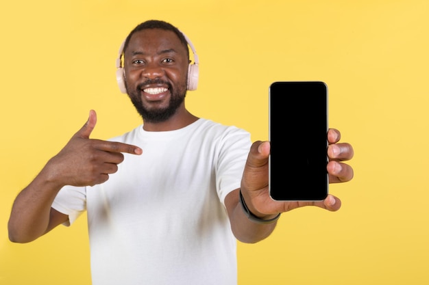 Hombre Afroamericano Mostrando Pantalla Del Teléfono Con Auriculares Sobre Fondo Amarillo