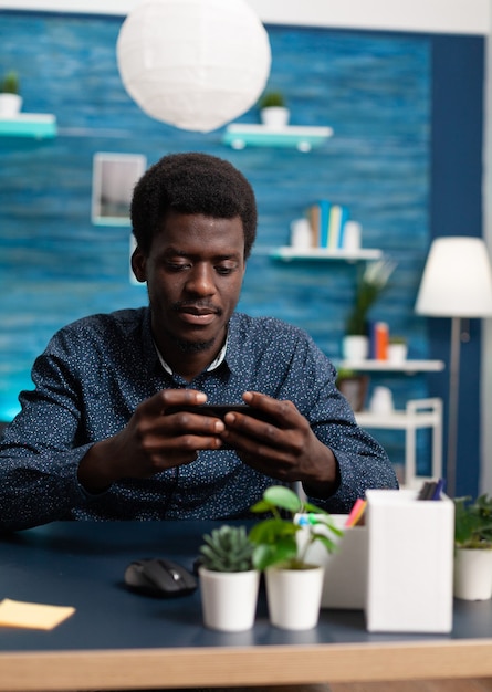Hombre afroamericano negro usando un teléfono inteligente en casa
