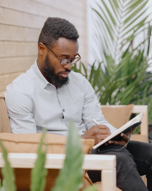 Hombre afroamericano en una oficina o coworking toma notas en un cuaderno y trabaja en una computadora portátil