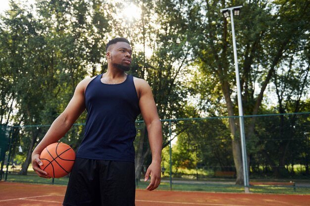 Hombre afroamericano de pie con pelota en la cancha al aire libre