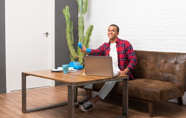 Hombre afroamericano con el portátil en la sala de estar hablando con un teléfono vintage