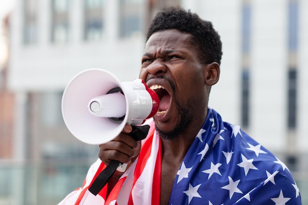 Hombre afroamericano con protestas de bandera de estados unidos y gritos en un megáfono