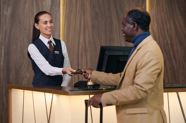 Hombre afroamericano recibiendo la llave de la habitación que se encuentra cerca de la recepción del hotel