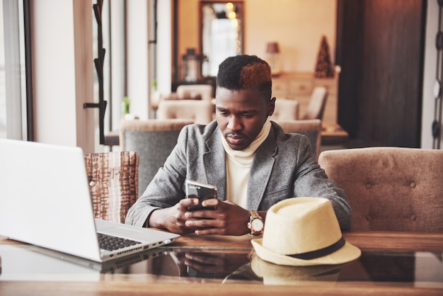 Hombre afroamericano sentado en un café y trabajando en una computadora portátil