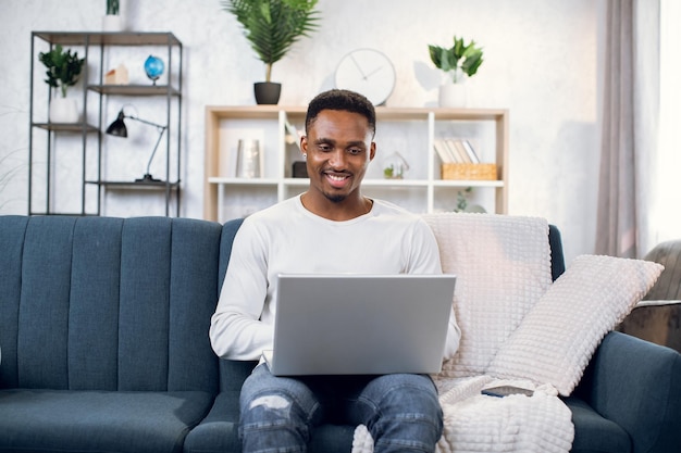 Hombre afroamericano sentado en el sofá y trabajando en una computadora portátil