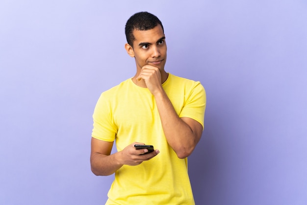 Hombre afroamericano sobre fondo púrpura aislado mediante teléfono móvil pensando en una idea