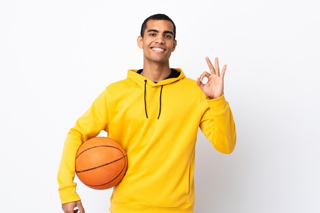 Hombre afroamericano sobre pared blanca aislada jugando baloncesto y haciendo firmar OK