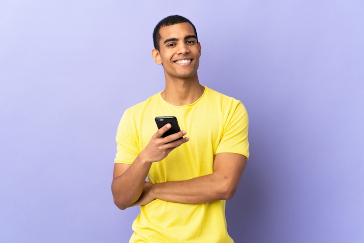 Foto hombre afroamericano sobre pared púrpura aislado usando teléfono móvil riendo