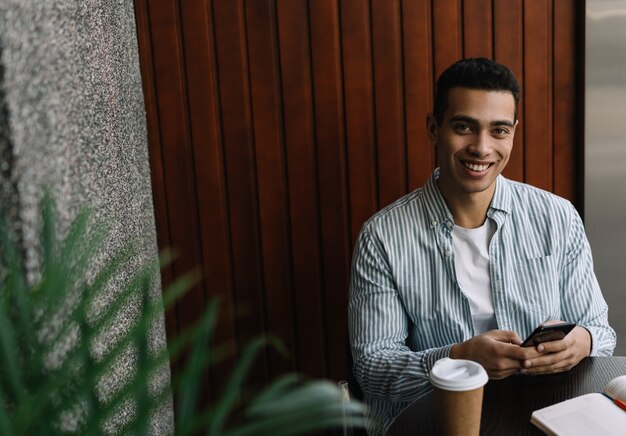 Hombre afroamericano sonriente hermoso que usa el teléfono móvil, comunicación, reservando en línea