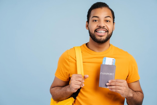 Hombre afroamericano sonriente con mochila de viaje y pasaporte con boletos de avión