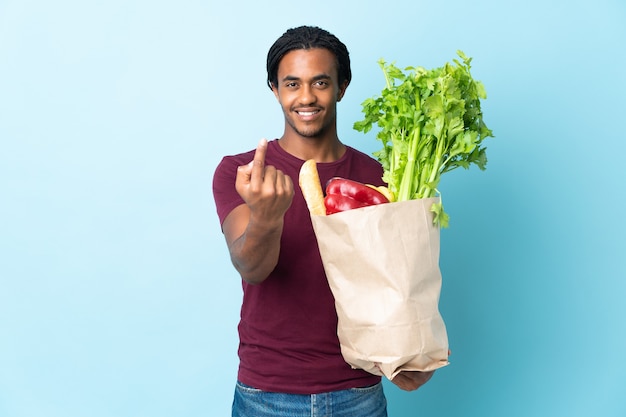 Hombre afroamericano sosteniendo una bolsa de compras en azul haciendo el gesto que viene