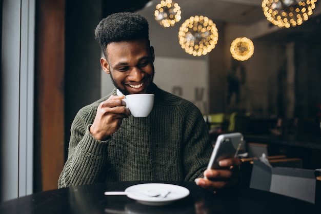 Hombre afroamericano con teléfono y café en un café