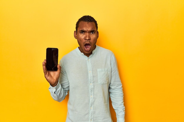 Hombre afroamericano con teléfono móvil estudio amarillo gritando muy enojado y agresivo