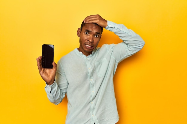 Foto hombre afroamericano con teléfono móvil estudio amarillo siendo conmocionado