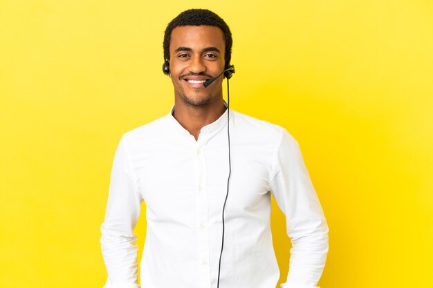 Hombre afroamericano Telemarketer trabajando con un auricular sobre fondo amarillo aislado riendo