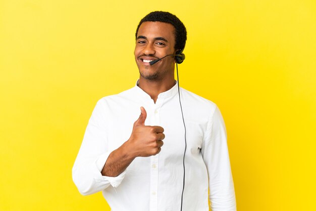 Hombre afroamericano Telemarketer trabajando con un auricular sobre pared amarilla aislada dando un gesto de pulgar hacia arriba