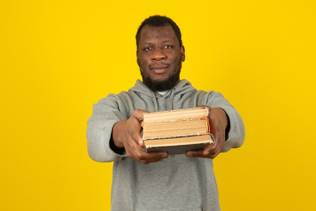 Hombre afroamericano tiene libros antiguos en la mano, se encuentra sobre la pared amarilla.