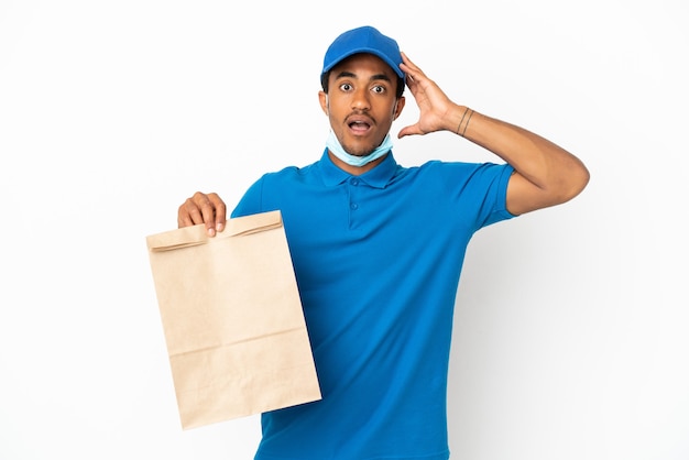 Hombre afroamericano tomando una bolsa de comida para llevar aislado sobre fondo blanco con expresión de sorpresa